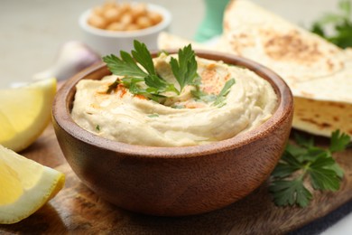 Photo of Delicious hummus with parsley, paprika, pita and lemon on table, closeup