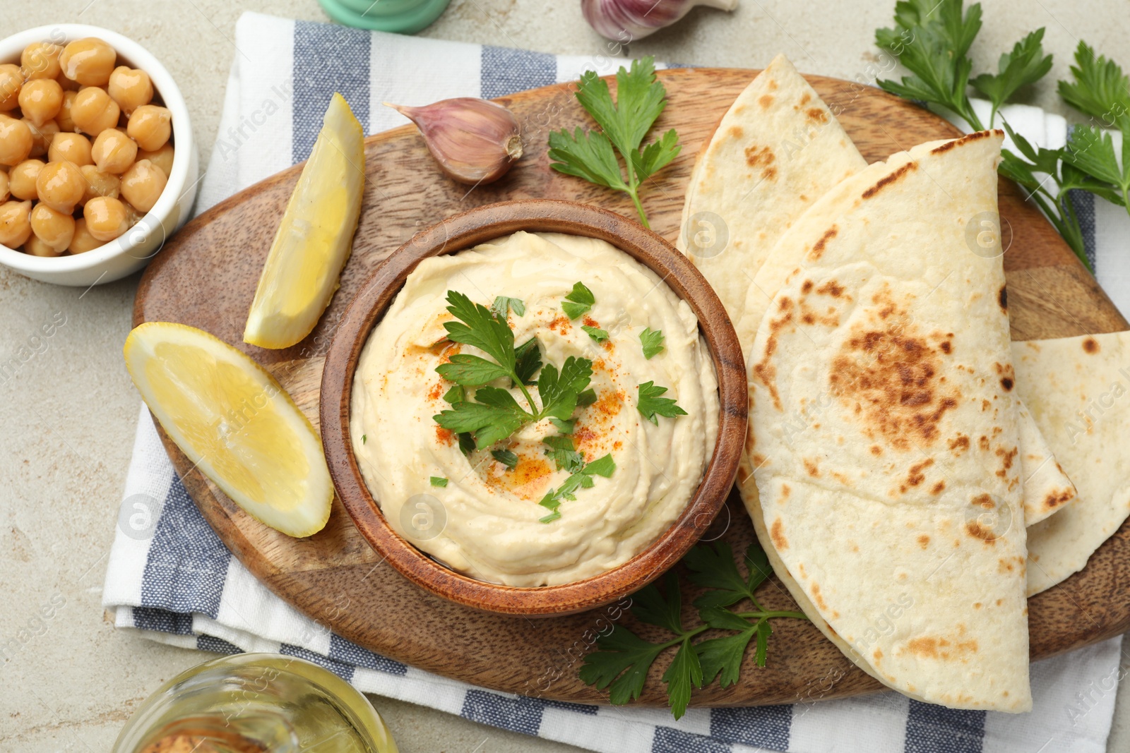 Photo of Delicious hummus with parsley, paprika, pita, chickpeas and lemon on grey table, top view