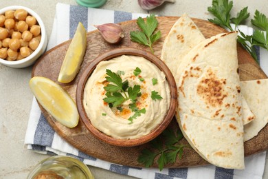 Photo of Delicious hummus with parsley, paprika, pita, chickpeas and lemon on grey table, top view