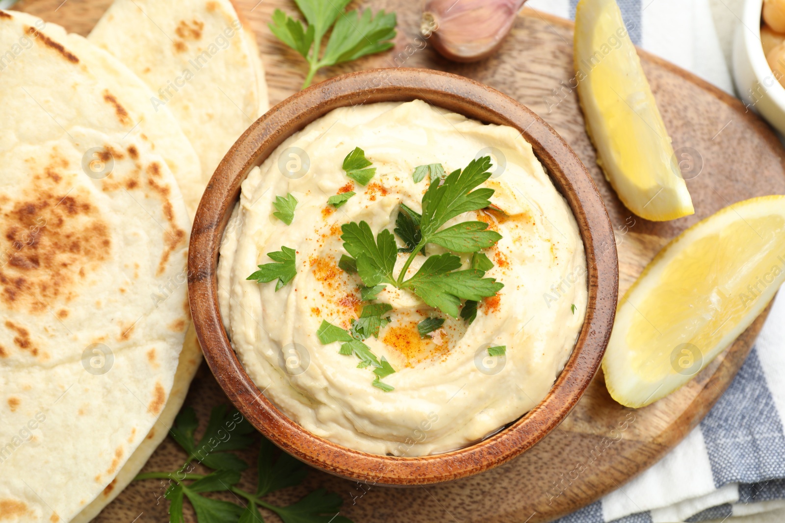 Photo of Delicious hummus with parsley, paprika, pita and lemon on table, top view