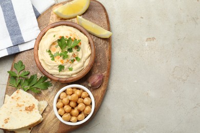 Photo of Delicious hummus with parsley, paprika, pita, chickpeas and lemon on grey table, top view. Space for text