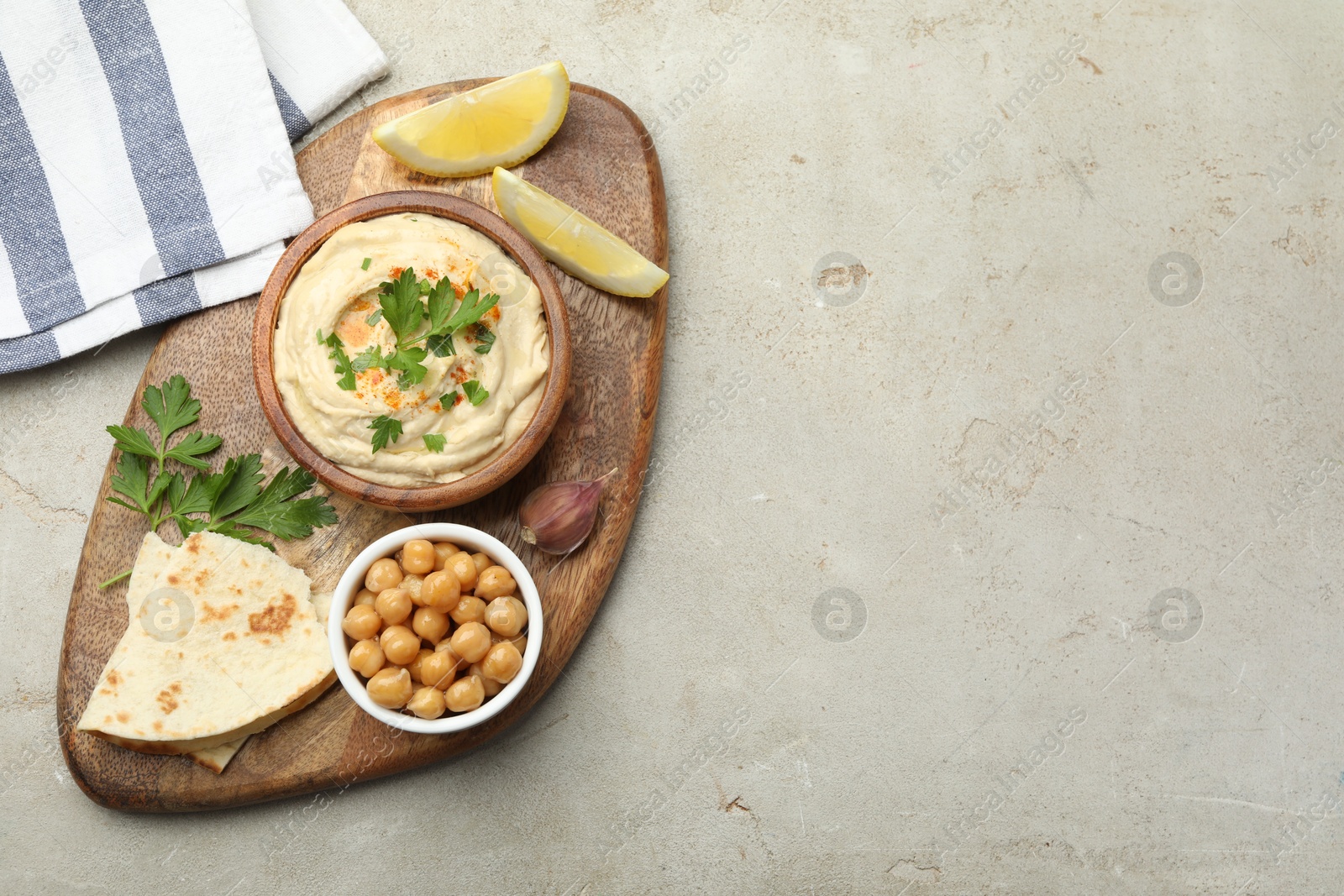 Photo of Delicious hummus with parsley, paprika, pita, chickpeas and lemon on grey table, top view. Space for text