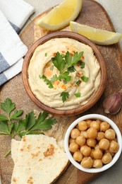 Photo of Delicious hummus with parsley, paprika, pita, chickpeas and lemon on table, top view