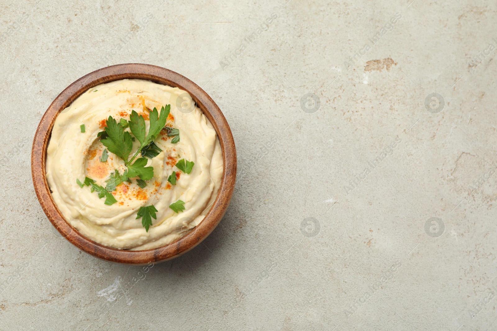 Photo of Delicious hummus with paprika and parsley in bowl on grey background, top view. Space for text