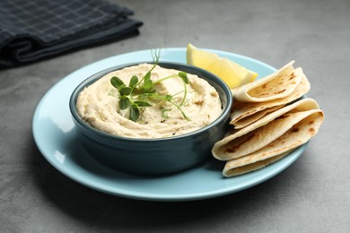 Photo of Delicious hummus in bowl, pita and lemon on grey table, closeup