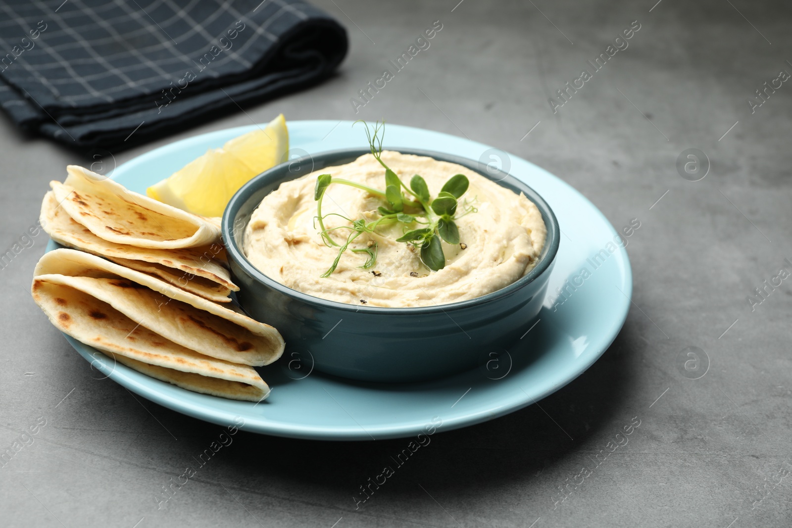 Photo of Delicious hummus in bowl, pita and lemon on grey table, closeup