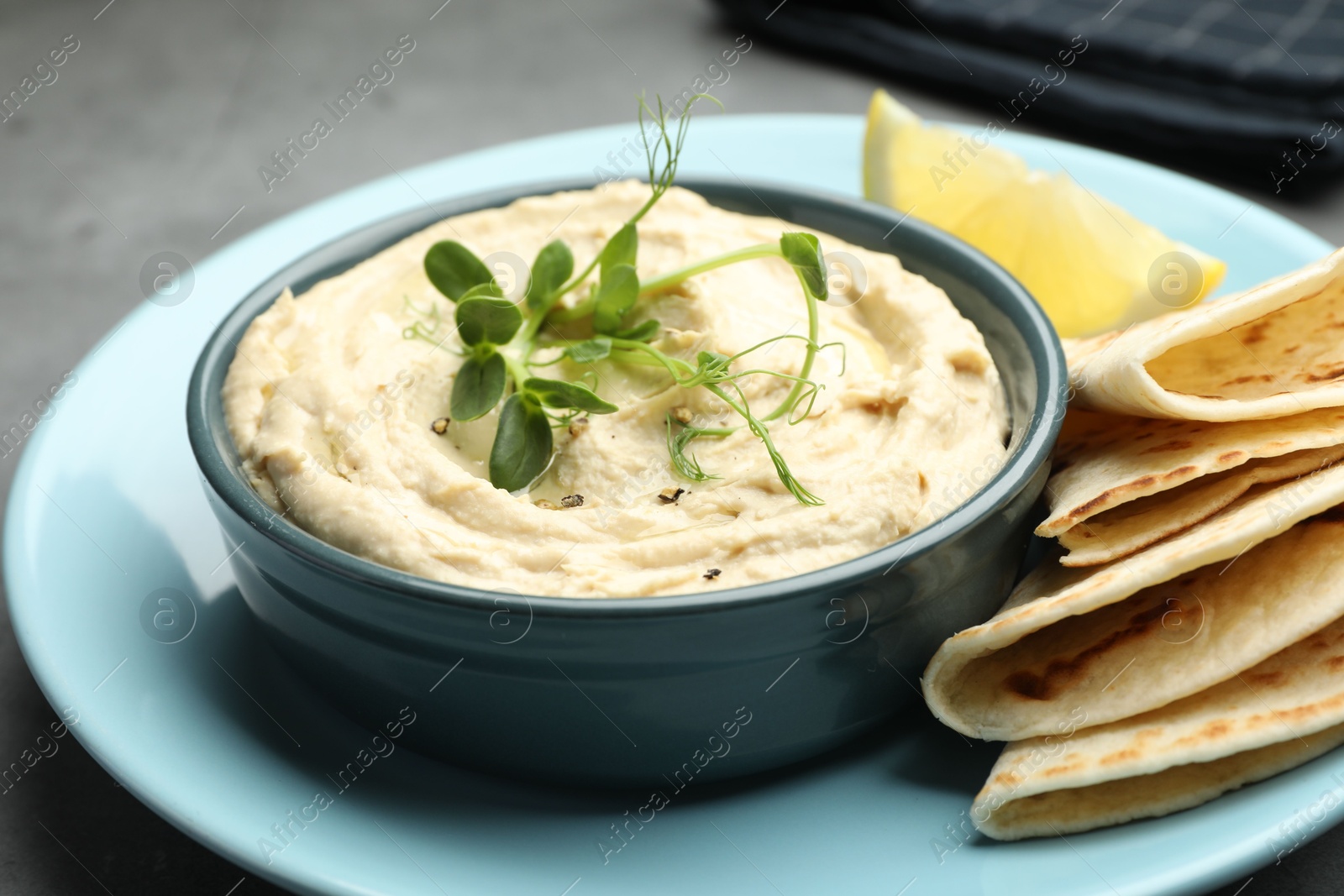 Photo of Delicious hummus in bowl, pita and lemon on table, closeup