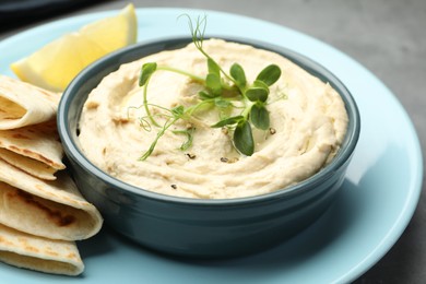 Photo of Delicious hummus in bowl, pita and lemon on table, closeup