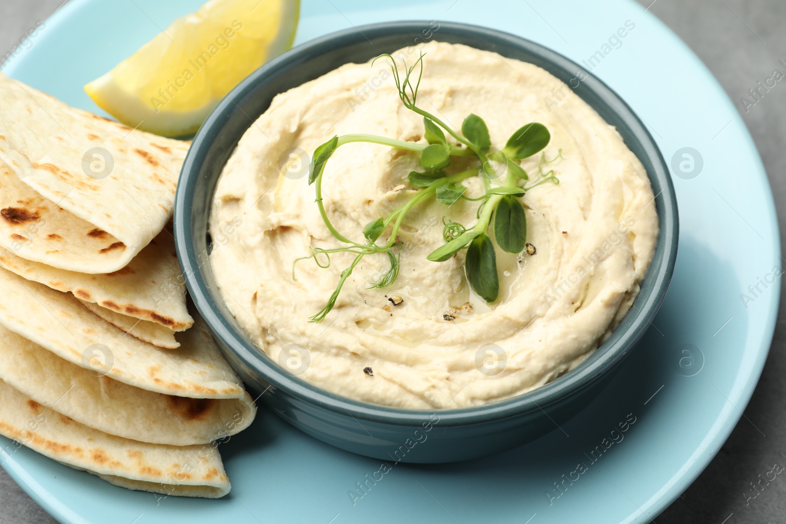 Photo of Delicious hummus in bowl, pita and lemon on table, closeup