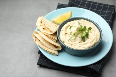 Photo of Delicious hummus in bowl, pita and lemon on grey table, space for text