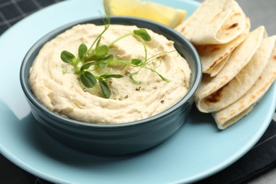 Photo of Delicious hummus in bowl, pita and lemon on table, closeup