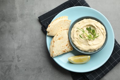 Photo of Delicious hummus in bowl, pita and lemon on grey table, top view. Space for text