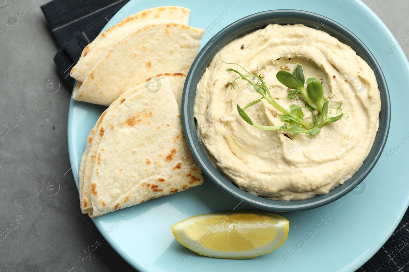 Photo of Delicious hummus in bowl, pita and lemon on grey table, top view