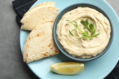 Photo of Delicious hummus in bowl, pita and lemon on grey table, top view