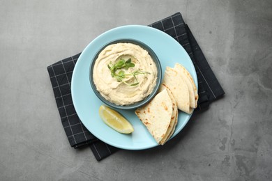 Delicious hummus in bowl, pita and lemon on grey table, top view