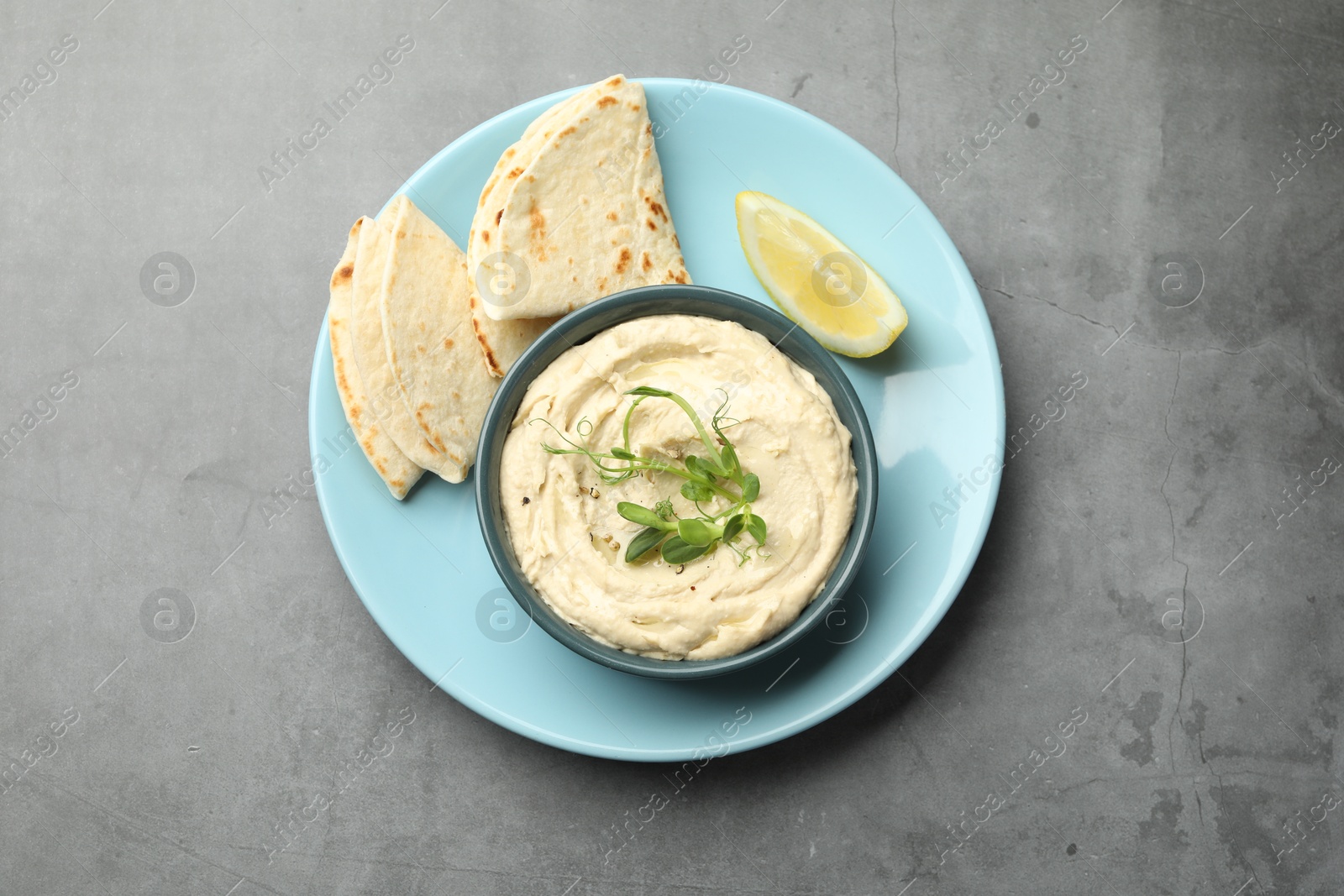 Photo of Delicious hummus in bowl, pita and lemon on grey table, top view