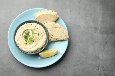 Photo of Delicious hummus in bowl, pita and lemon on grey table, top view. Space for text