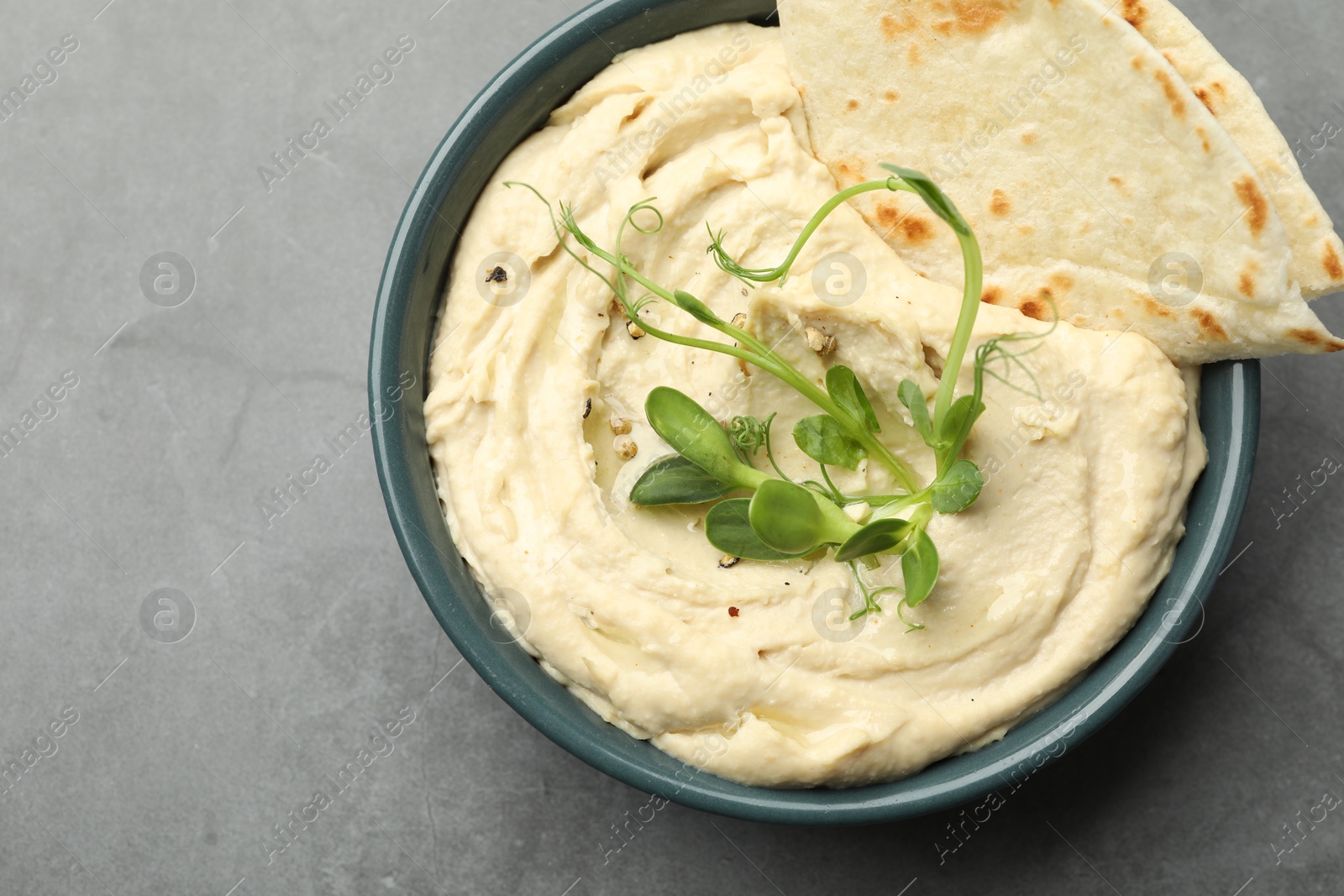 Photo of Delicious hummus in bowl and pita on grey table, top view