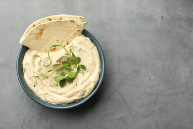 Delicious hummus in bowl and pita on grey table, top view. Space for text