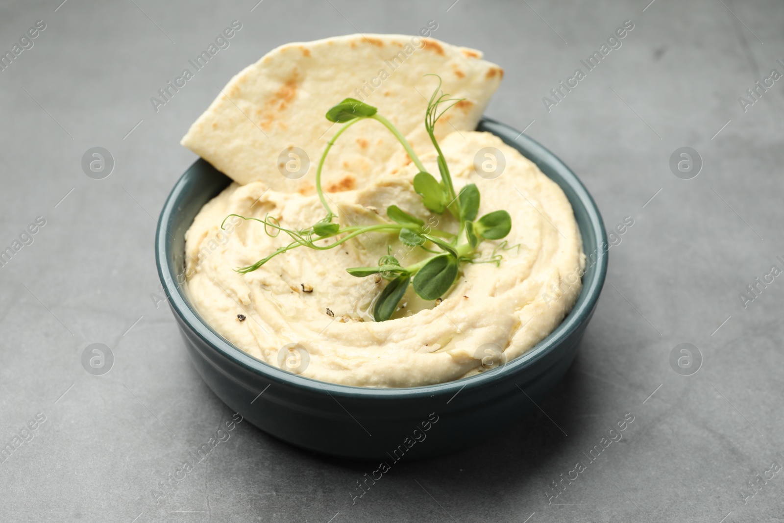 Photo of Delicious hummus in bowl and pita on grey table, closeup