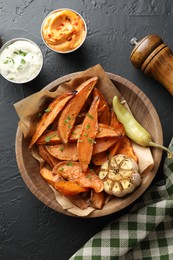 Photo of Tasty cooked sweet potatoes with garlic, pickled pepper and sauces on black table, top view