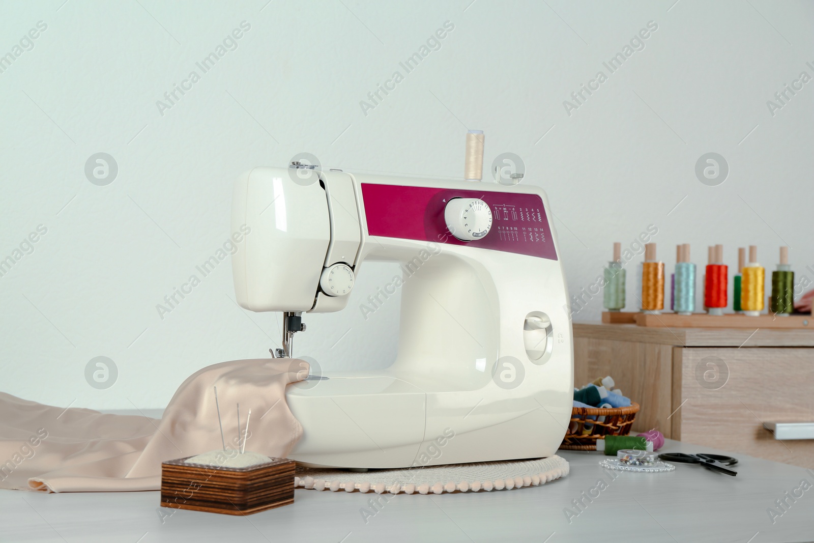 Photo of Sewing machine, beige fabric and craft accessories on wooden table indoors