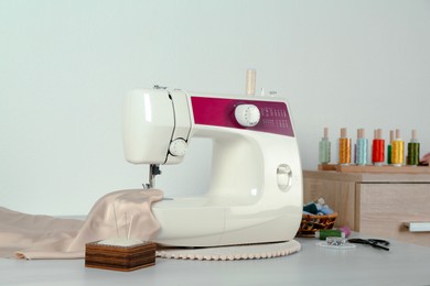 Sewing machine, beige fabric and craft accessories on wooden table indoors