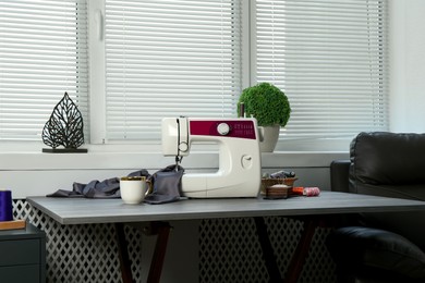 Sewing machine, gray fabric and craft accessories on wooden table indoors