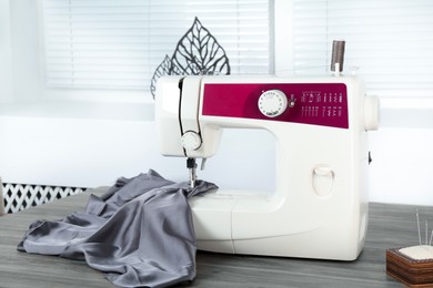 Photo of Sewing machine with gray fabric on wooden table indoors