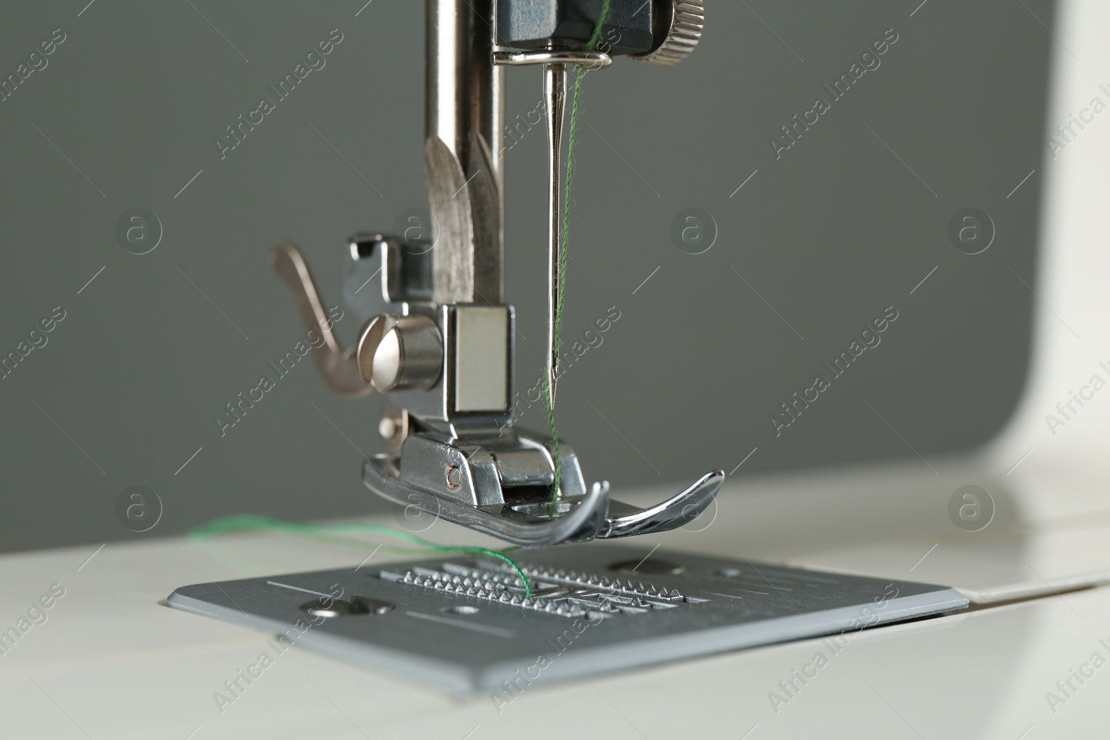 Photo of Sewing machine with green thread on grey background, closeup