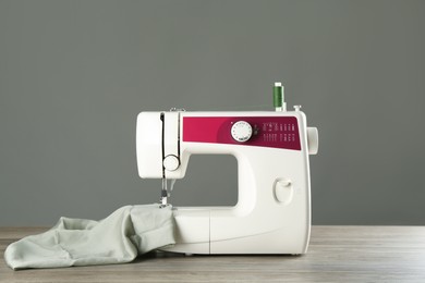 Photo of One sewing machine with fabric on wooden table against grey background