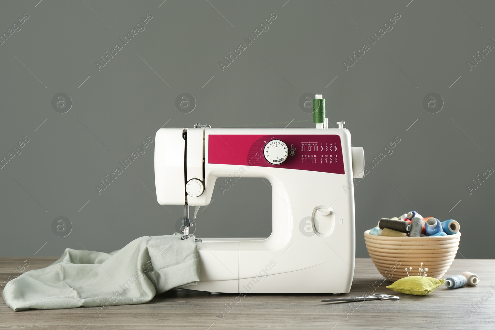 Photo of Sewing machine with fabric and tools on wooden table against grey background