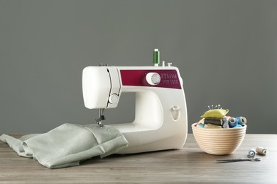 Sewing machine with fabric and tools on wooden table against grey background