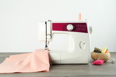 Photo of One sewing machine with fabric and tools on wooden table against white background