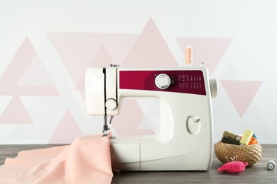 Photo of One sewing machine with fabric and tools on wooden table indoors