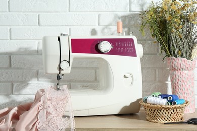 Photo of Sewing machine with fabric, flowers in vase and tools on wooden table indoors