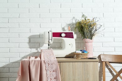 Chest of drawers with sewing machine, fabric, flowers in vase and tools at workshop