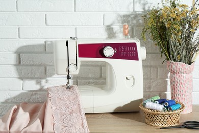 Sewing machine with fabric, flowers in vase and tools on wooden table indoors