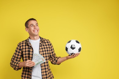 Happy man with money and soccer ball on yellow background, space for text