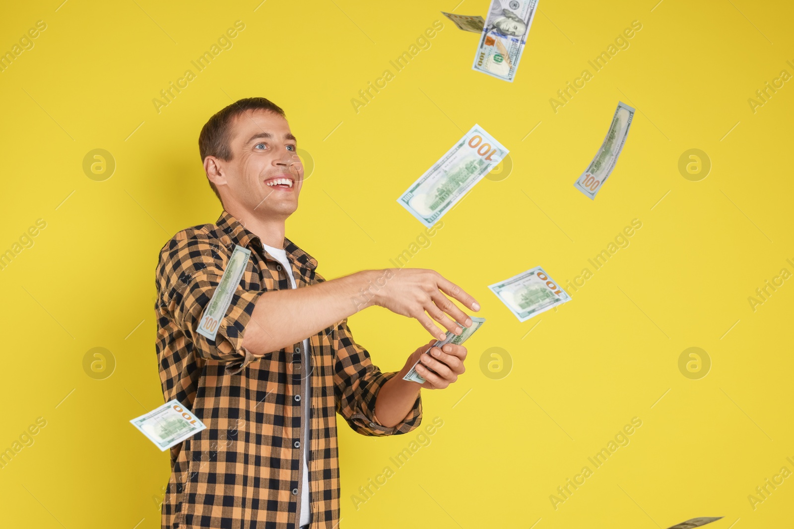 Photo of Happy man throwing money on yellow background, space for text