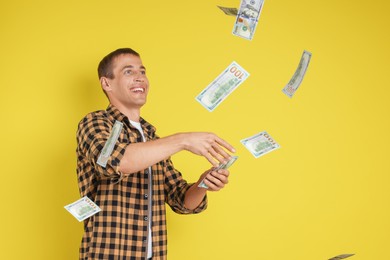 Photo of Happy man throwing money on yellow background, space for text