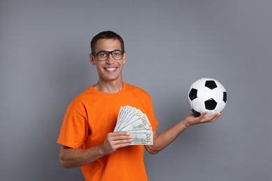 Happy man with money and soccer ball on grey background