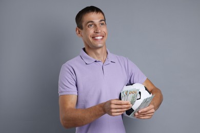 Man with money and soccer ball on grey background