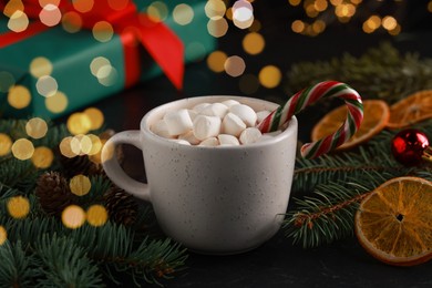 Photo of Tasty hot cocoa drink with marshmallows, candy cane in cup and Christmas decor on table, closeup