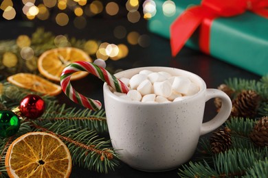 Photo of Tasty hot cocoa drink with marshmallows, candy cane in cup and Christmas decor on table, closeup