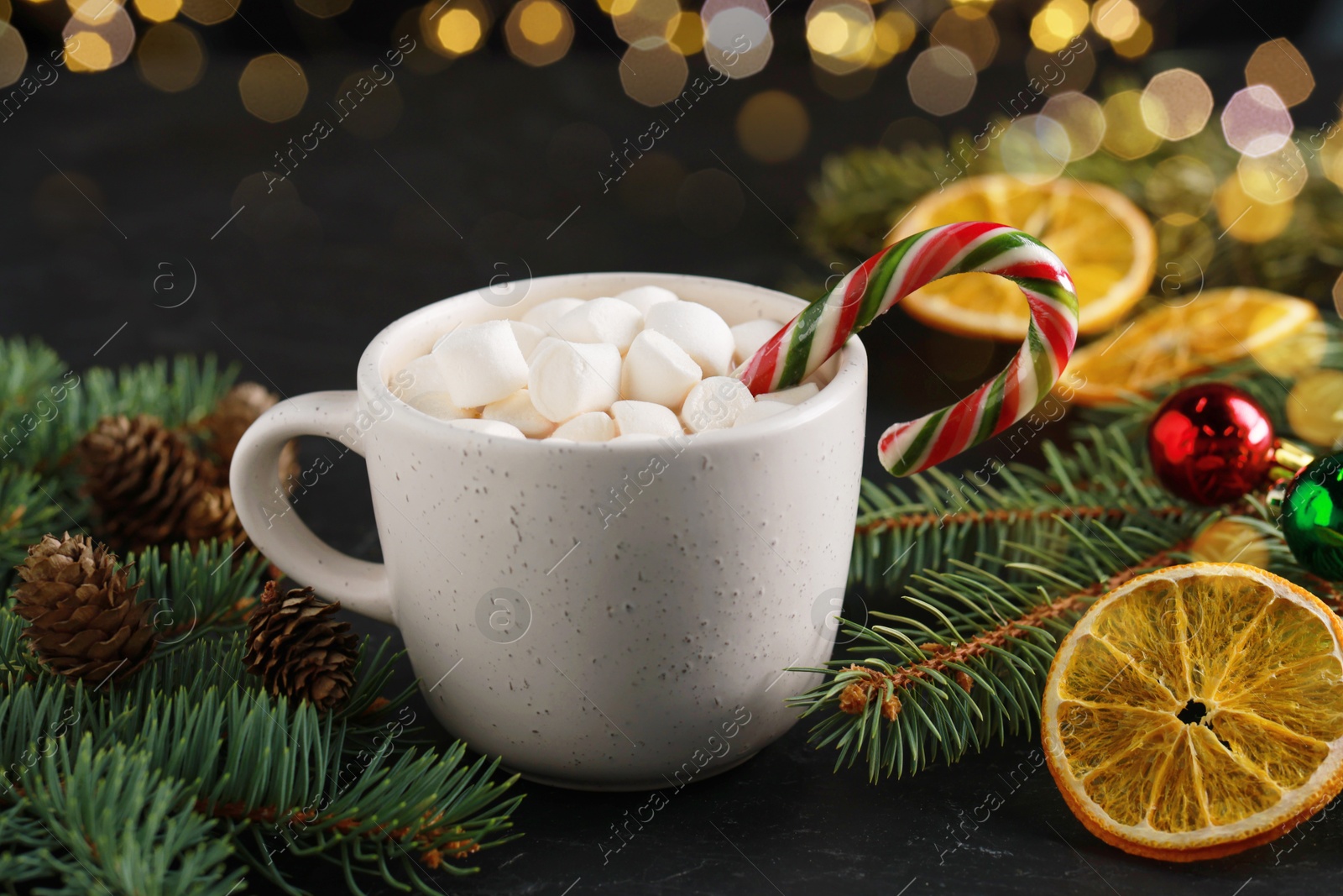 Photo of Tasty hot cocoa drink with marshmallows, candy cane in cup and Christmas decor on table, closeup