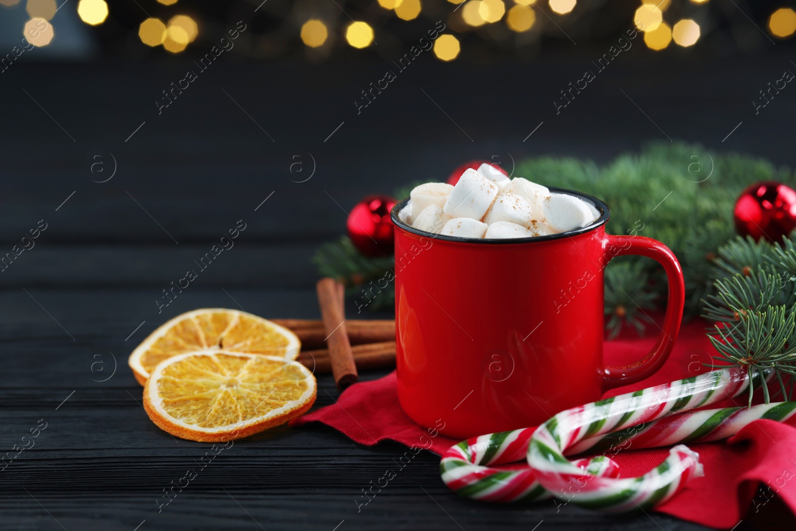 Photo of Tasty hot cocoa drink with marshmallows in mug, candy canes and Christmas decor on black wooden table, closeup. Space for text