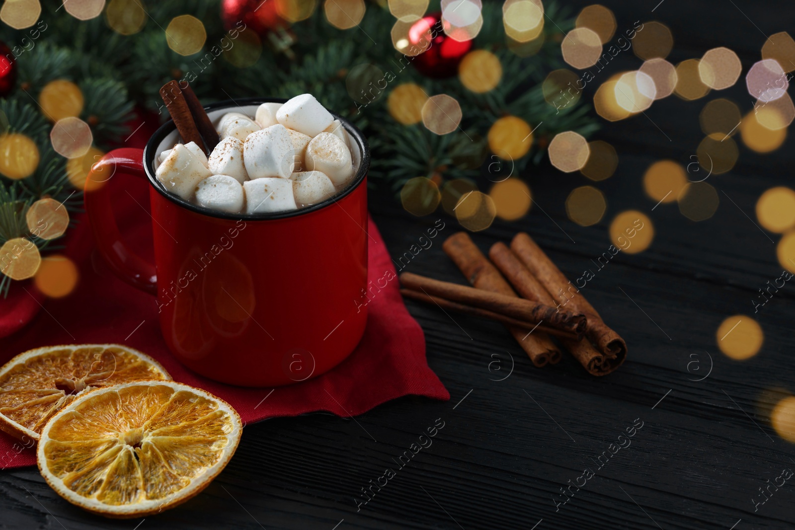 Photo of Tasty hot cocoa drink with marshmallows in mug and spices on black wooden table, closeup