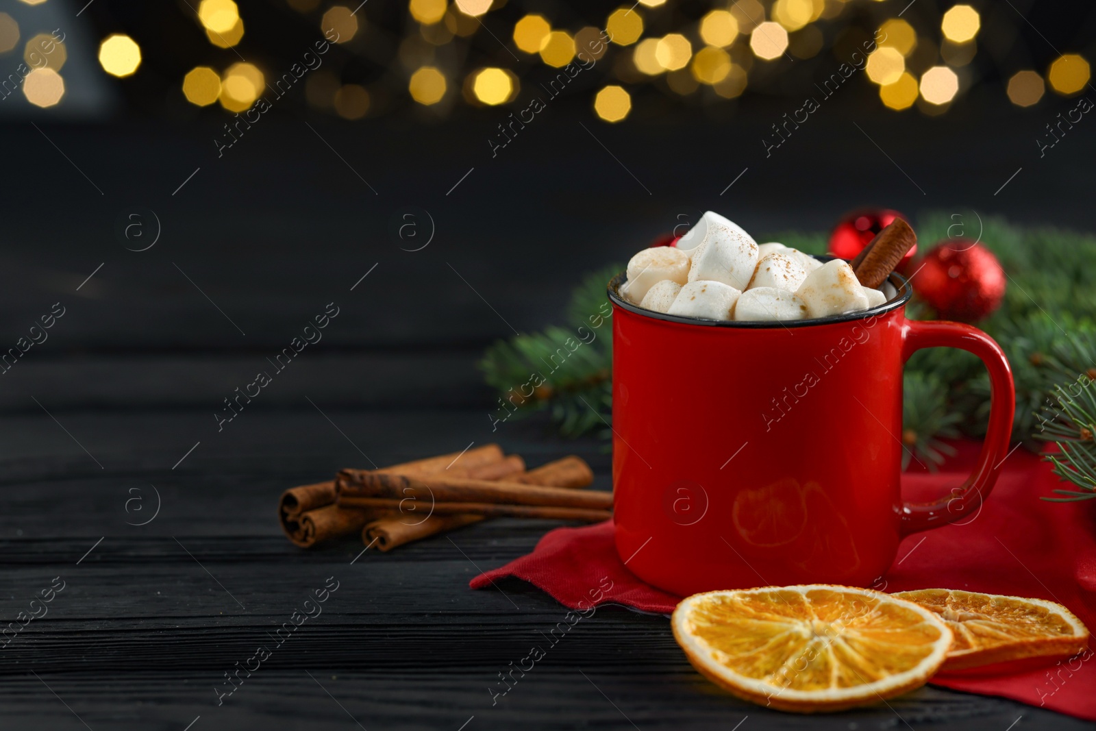 Photo of Tasty hot cocoa drink with marshmallows in mug and spices on black wooden table, closeup. Space for text