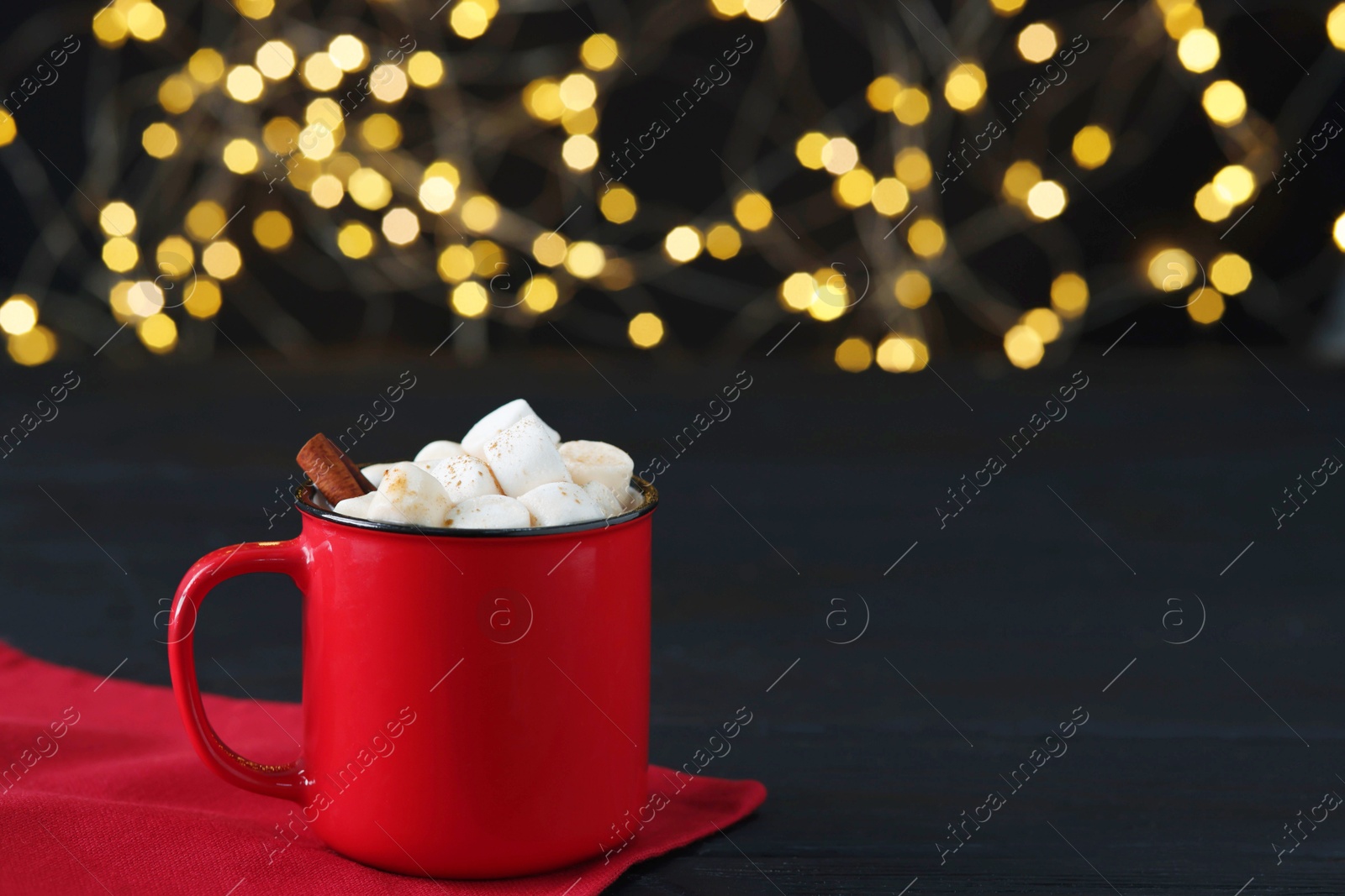 Photo of Tasty hot cocoa drink with marshmallows and cinnamon sticks in mug on black wooden table, closeup. Space for text